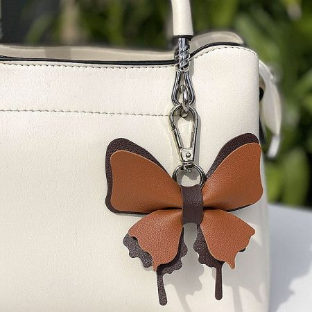 A white handbag featuring a brown butterfly-shaped faux leather charm.