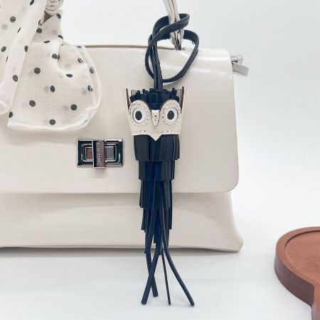 Black leather owl keychain with tassel charm attached to a stylish white handbag.