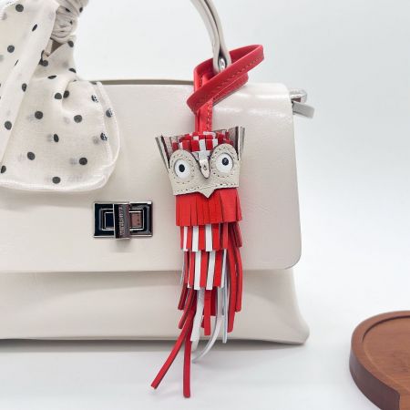 Red leather owl keychain with tassel charm accenting a chic white leather bag.