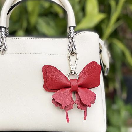 Red faux leather bow charm clipped onto a white handbag.