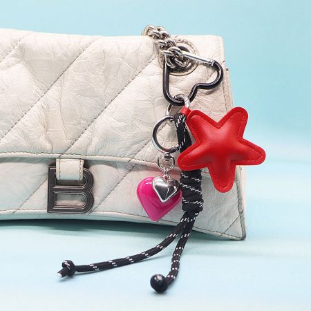 A red PU leather heart keychain with a matching rope strap and pink heart charm attached to a white purse.