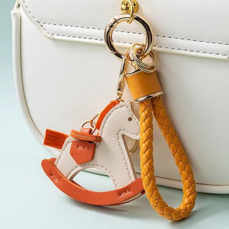 Tangerine-colored pony keychain adding a pop of color to a white leather purse.