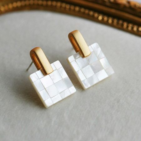 A pair of unique white mosaic earrings with a striking gold frame.