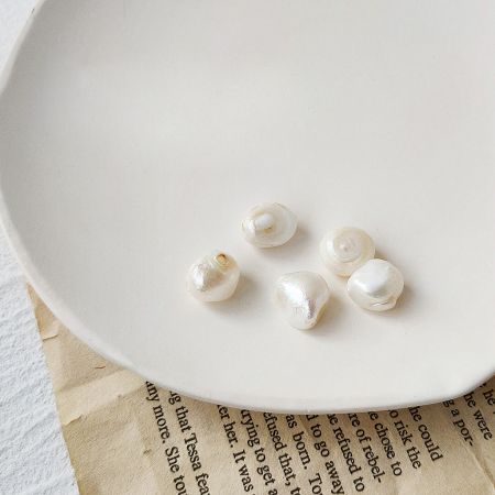 Loose natural freshwater pearls on a ceramic plate, highlighting their unique shapes.