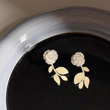 Product lifestyle photo of the white rose stud earrings presented in a silver bowl on a reflective surface.