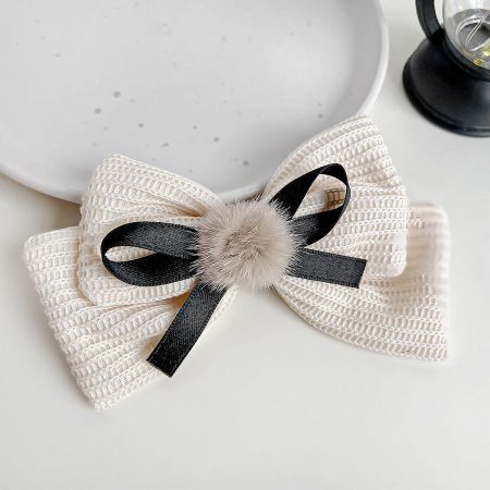 A stylish white textured fabric bow accented with a black ribbon and a playful pom-pom.