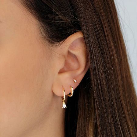A close-up view of a gold stud and hoop earring worn on a model's ear.