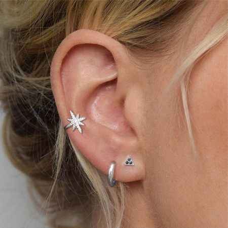 A woman's ear showing the silver starburst ear cuff along with other silver earrings.