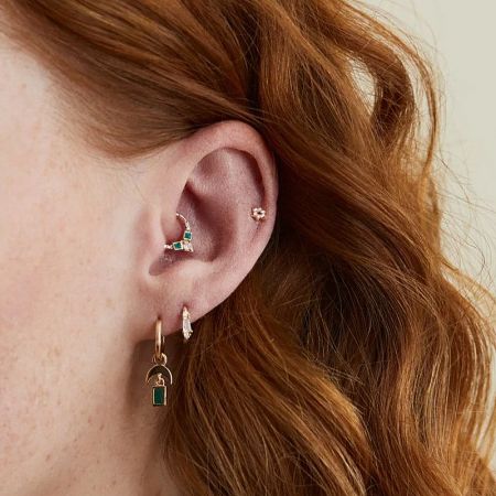 A model's ear adorned with the geometric green zircon cartilage earring and other jewelry.