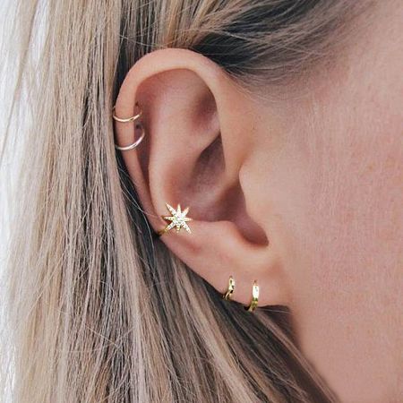 A woman's ear adorned with a gold starburst ear cuff and other hoop earrings.