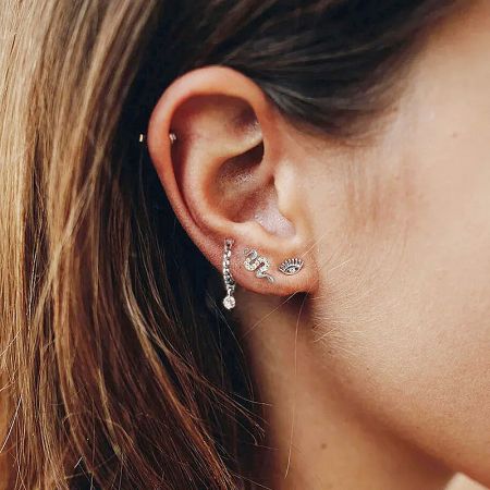 A model's ear adorned with multiple piercings and a collection of delicate sterling silver stud earrings.