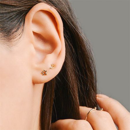 A woman's ear adorned with the star stud earring and a crescent moon earring, showcasing a stylish combination.