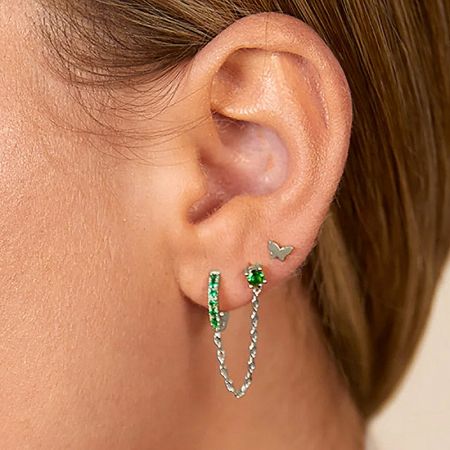 A model wearing the silver version of the earring set, highlighting a butterfly stud and green gemstone accents.