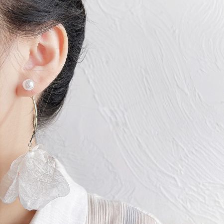 A woman modeling the asymmetrical earring set, featuring a pearl stud and a gold hoop with a white petal pendant.