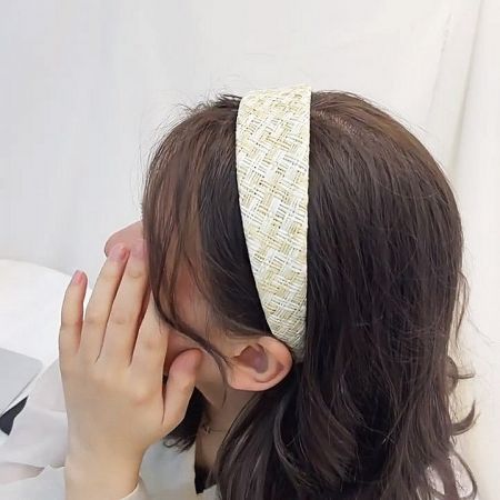 A woman with brown hair models a stylish hand-woven raffia headband, showcasing its bohemian look.