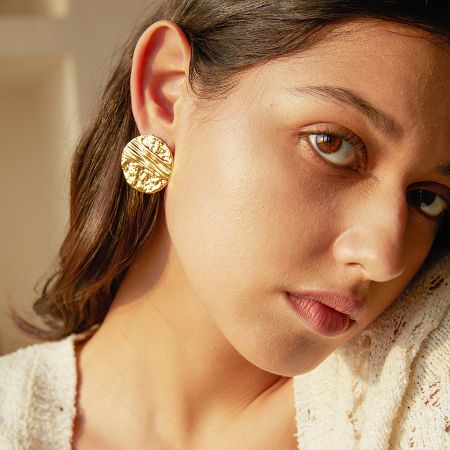 A model showcasing the stylish appeal of the gold hammered disc stud earrings.