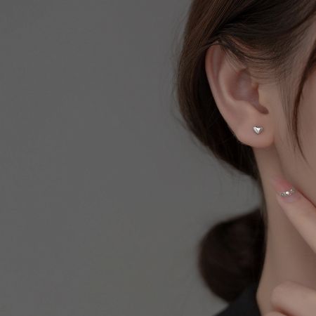 A woman showcasing a delicate silver heart stud earring.