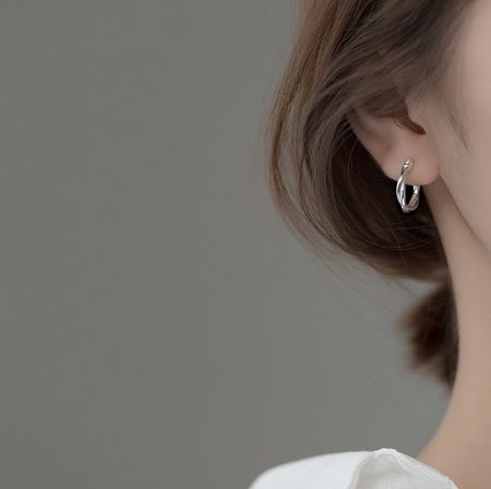 A close-up view of the silver twisted hoop earring being worn, showcasing its size and style on the ear.