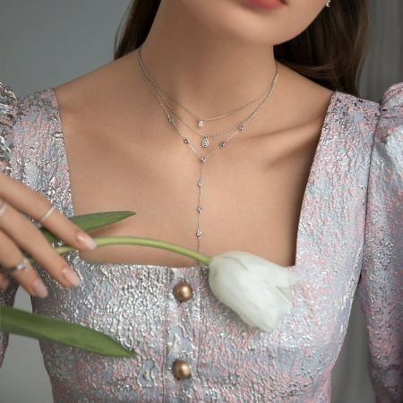 925 Sterling Silver Wholesale CZ Y Necklace Silver Layered Everyday Jewelry Set of 5 - A model wearing the wholesale 925 sterling silver cubic zirconia Y necklace set, showcasing its layered style against a pink top while holding a white tulip.