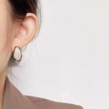 Model showcasing a unique white translucent stone earring with an irregular gold frame.