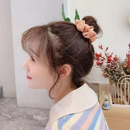 A model showcasing a pink fabric scrunchie in her hair bun, demonstrating its use.