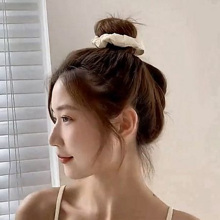 A woman with a stylish bun held in place by a chic white silk scrunchie.