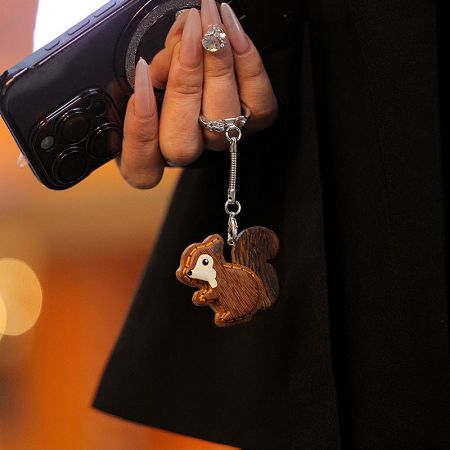 A charming wooden squirrel keychain attached to a smartphone, demonstrating its use as a phone charm.
