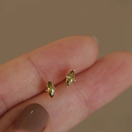 A hand holding the delicate gold-plated sterling silver stud earring to display its size and vibrant olive green stone.