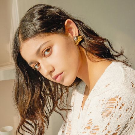 Model showcasing the gold chunky weave triangle earrings, complementing her stylish white top.