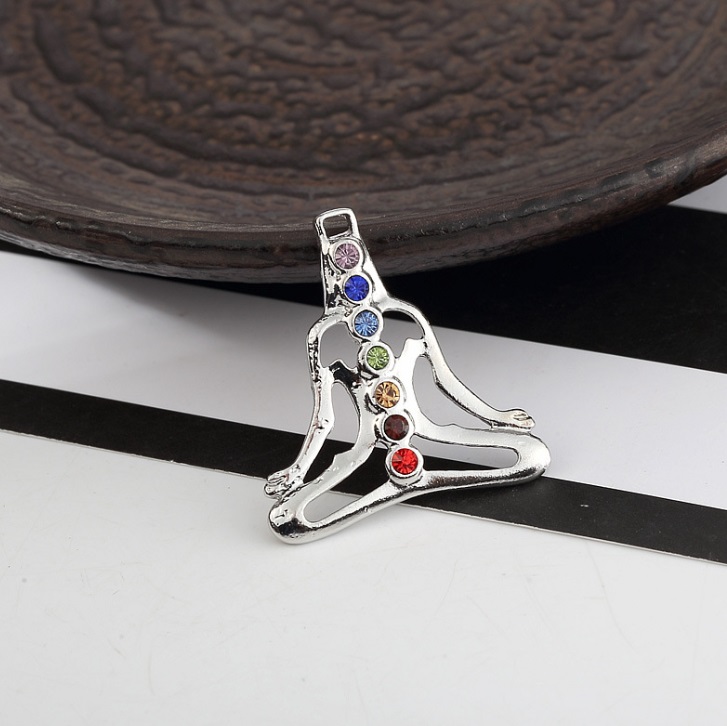 A silver pendant depicting a meditating figure with seven vertically aligned colored gemstones representing the chakras, symbolizing spiritual balance.