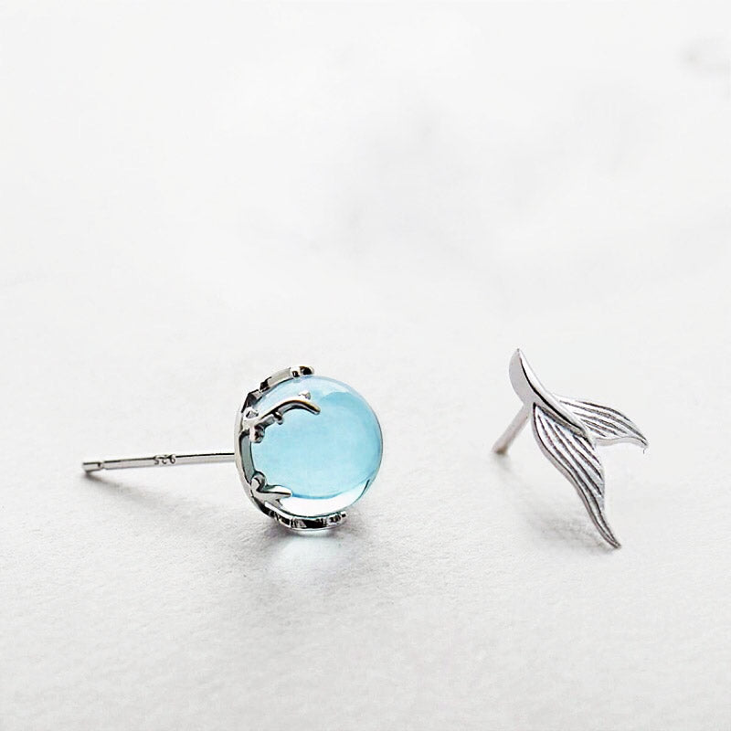 A pair of asymmetrical 925 sterling silver stud earrings, one featuring a round moonstone and the other a detailed mermaid fishtail, on a clean white background.