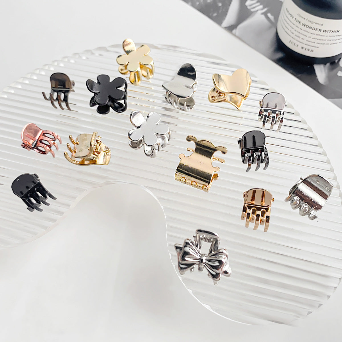 A diverse collection of mini metal alloy hair claw clips in various shapes like flowers and bows, and colors including gold, silver, and black.