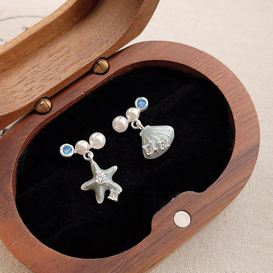 A collection of ocean-themed earrings from JR Fashion Accessories, featuring delicate silver starfish and seashell charms with pearl and zircon details, representing the wholesale ocean jewelry line.