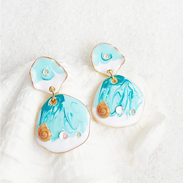 A complete set of five pairs of ocean-beach style drop earrings, showcasing various designs with hand-painted enamel, seashells, and 14k gold accents on a white background.
