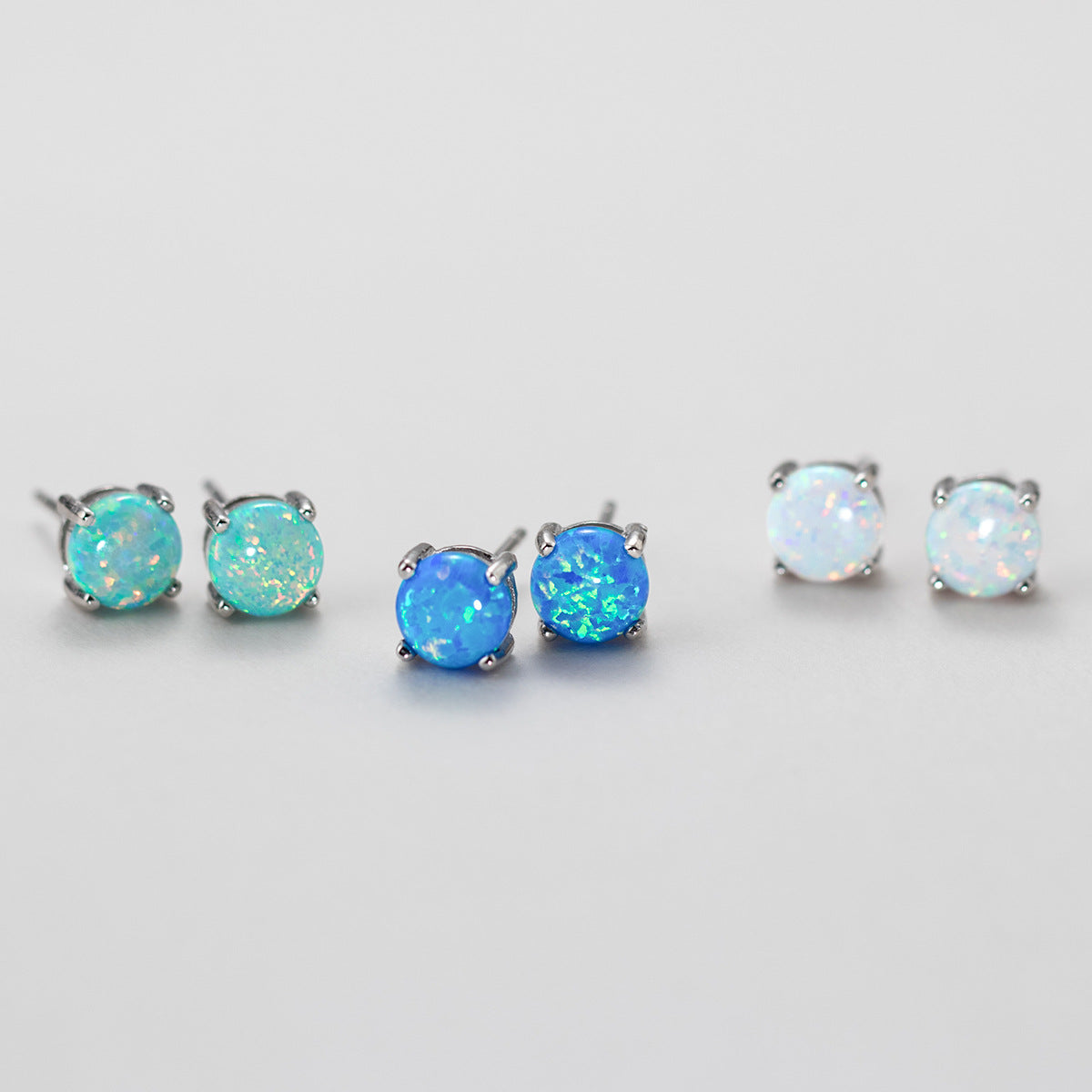 Three pairs of 925 sterling silver opal stud earrings showcasing the color options: dreamy light blue, ocean blue, and pure white.
