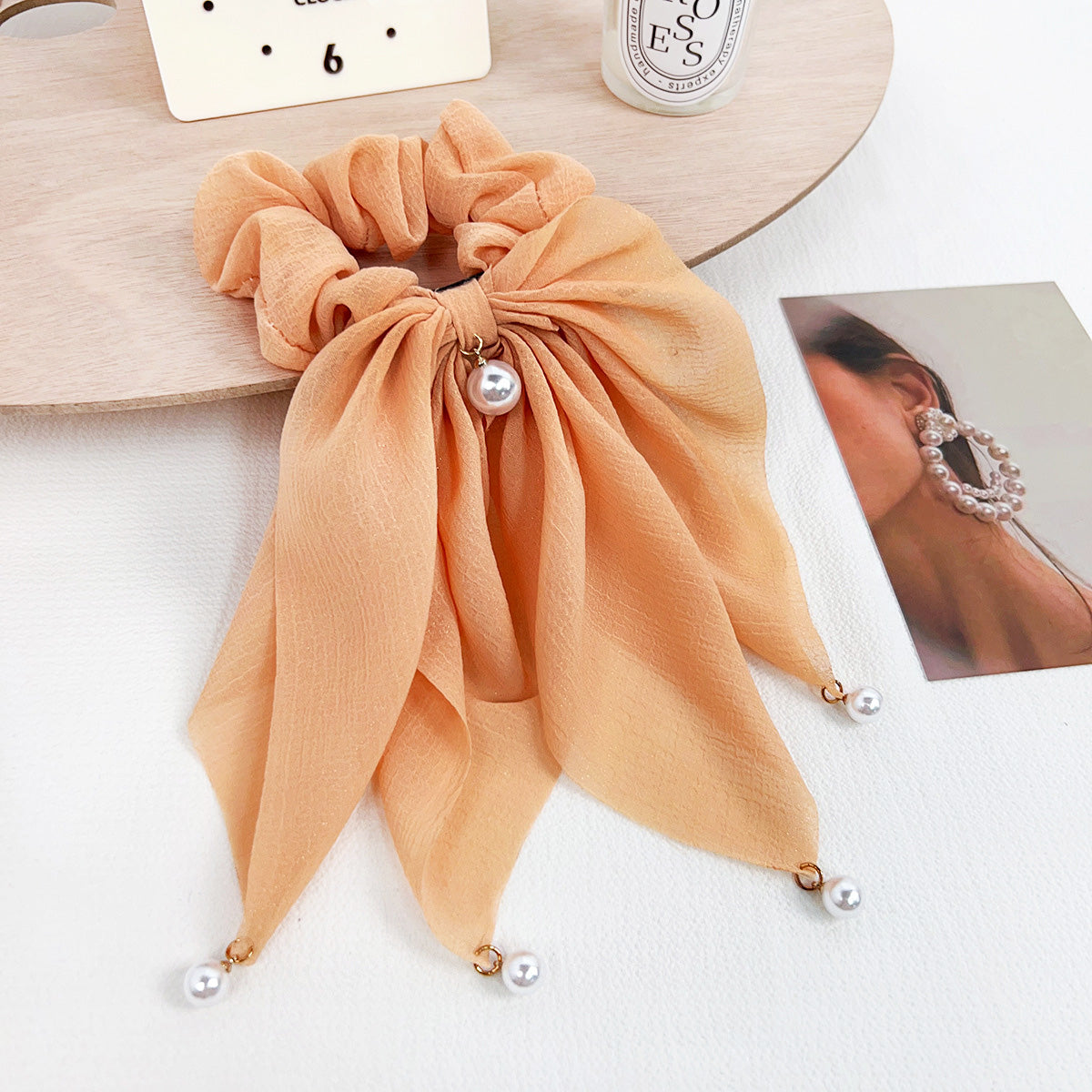 A close-up of a trendy peach-colored Japanese style ruffle hair scrunchie, elegantly detailed with a delicate pearl ribbon.