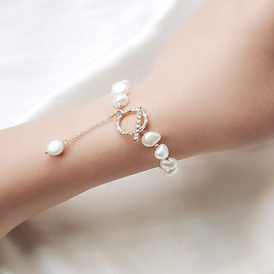 A model's wrist adorned with an elegant 14k gold-plated baroque freshwater pearl bracelet, featuring a secure toggle clasp. Part of a set of five.