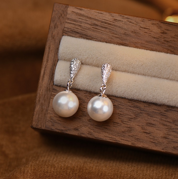 A pair of elegant 925 sterling silver pearl dangle earrings with sparkling cubic zirconia tops, displayed in a wooden jewelry box.