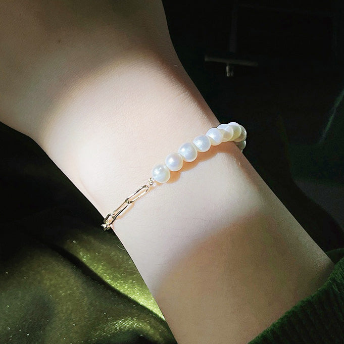 A model's wrist adorned with an elegant 14k gold-plated bracelet featuring freshwater pearls and a paper clip chain design.