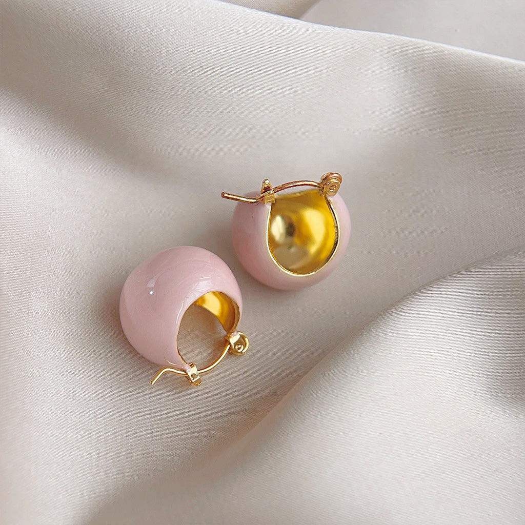 A close-up studio shot of the pink enamel and gold-plated bucket hoop stud earrings, showcasing their spherical shape and hinged design.