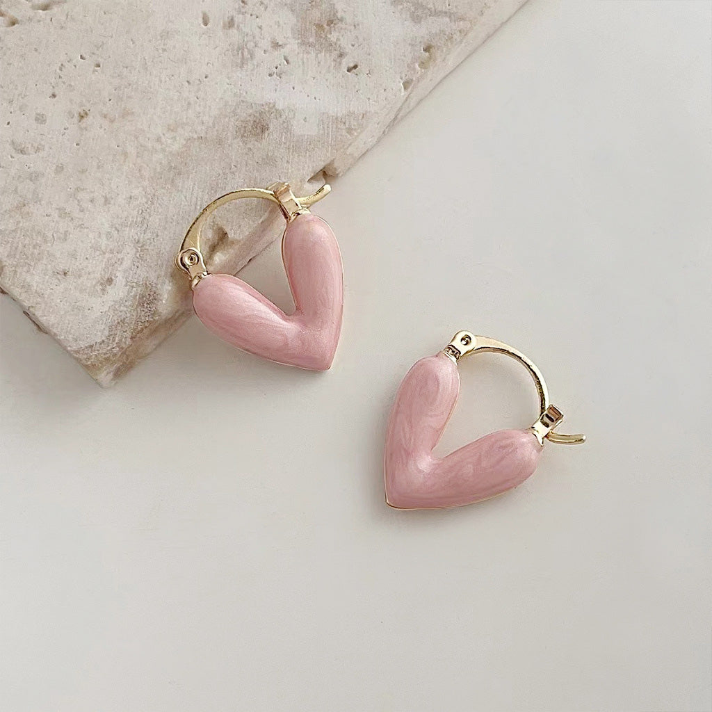 A pair of 14k gold-plated heart hoop earrings with vibrant double-sided pink enamel, showcasing the detailed craftsmanship and gold clasps.