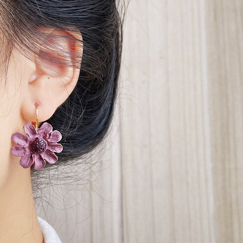 A model wearing a vibrant purple enamel 3D flower earring with a gold French hook, showcasing its elegant design and fit.