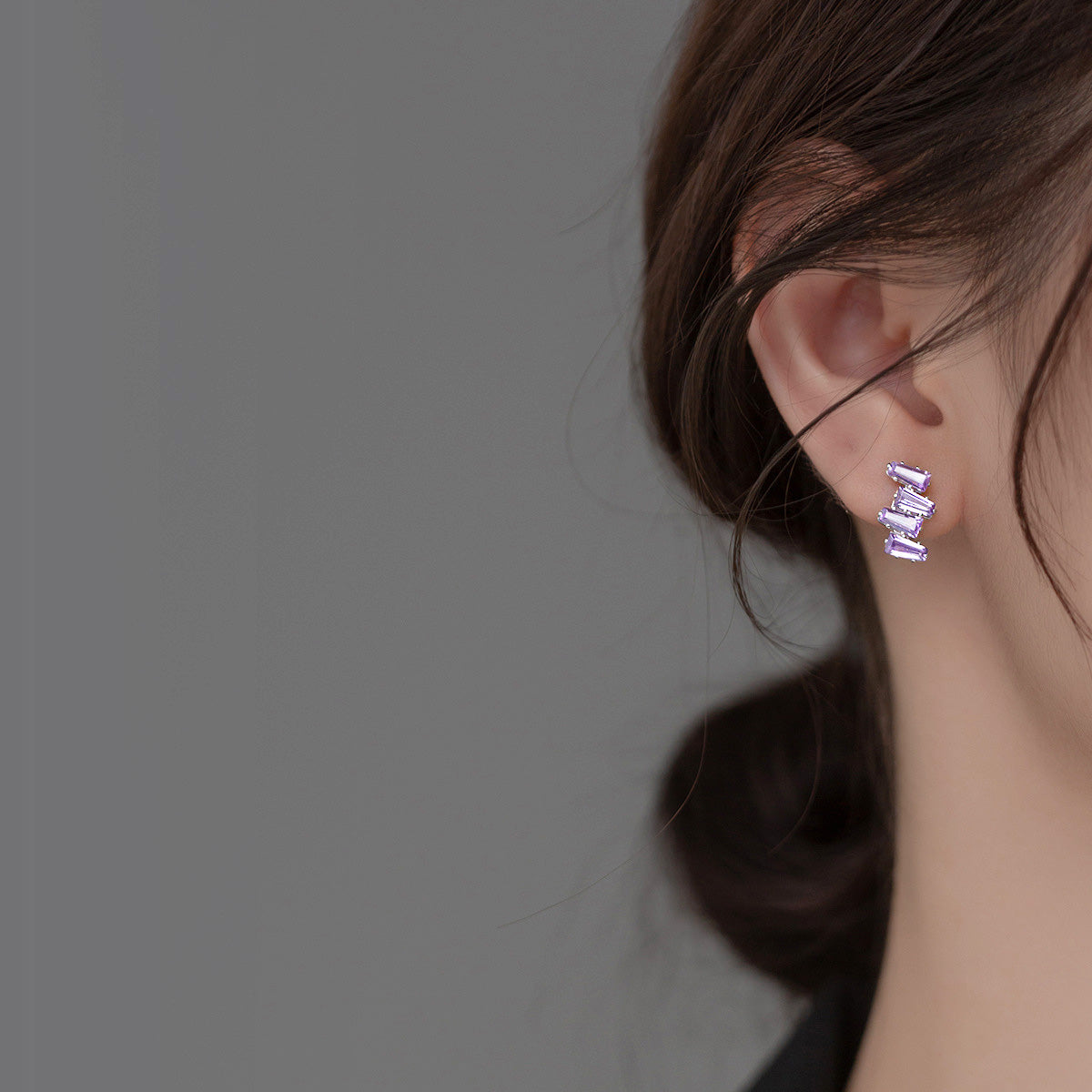 Close-up of a woman wearing elegant 925 sterling silver stud earrings with vibrant purple crystal jagged baguette stones.