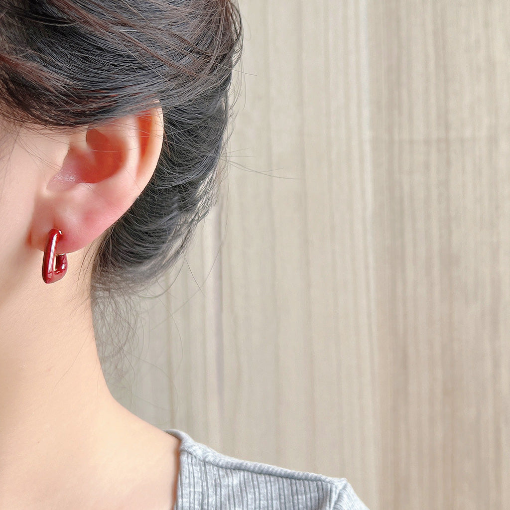 Close-up of a 14k gold plated C-shape stud earring with a vibrant red enamel finish.