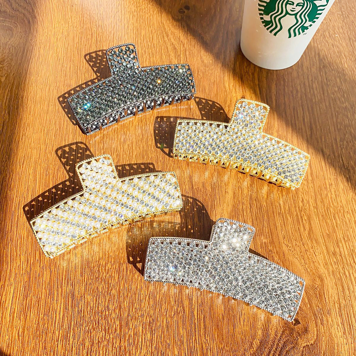A set of five large metal alloy hair claw clips, studded with sparkling rhinestones in silver and gold, elegantly arranged on a wooden surface.