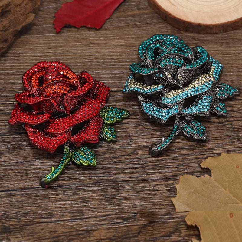 A pair of luxurious rhinestone rose flower brooches, one in vibrant red and the other in elegant blue, displayed on a rustic wooden surface.