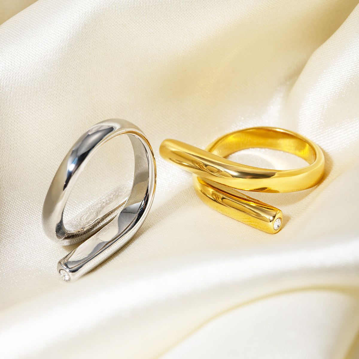 A set of stainless steel geometric rings with single CZ stones, displayed in both silver and gold finishes on a neutral background.