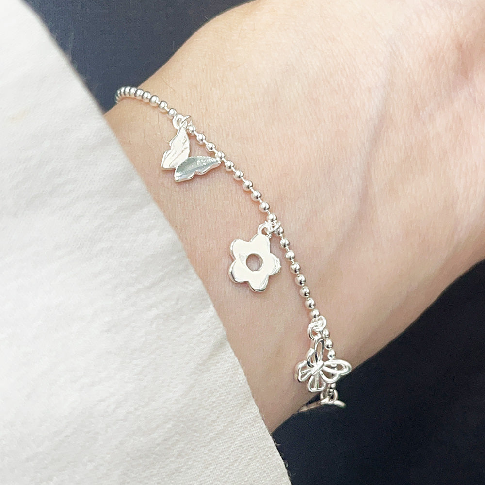 Close-up of a 925 sterling silver ball chain bracelet with delicate butterfly and flower charms, worn on a wrist. Part of a wholesale set.