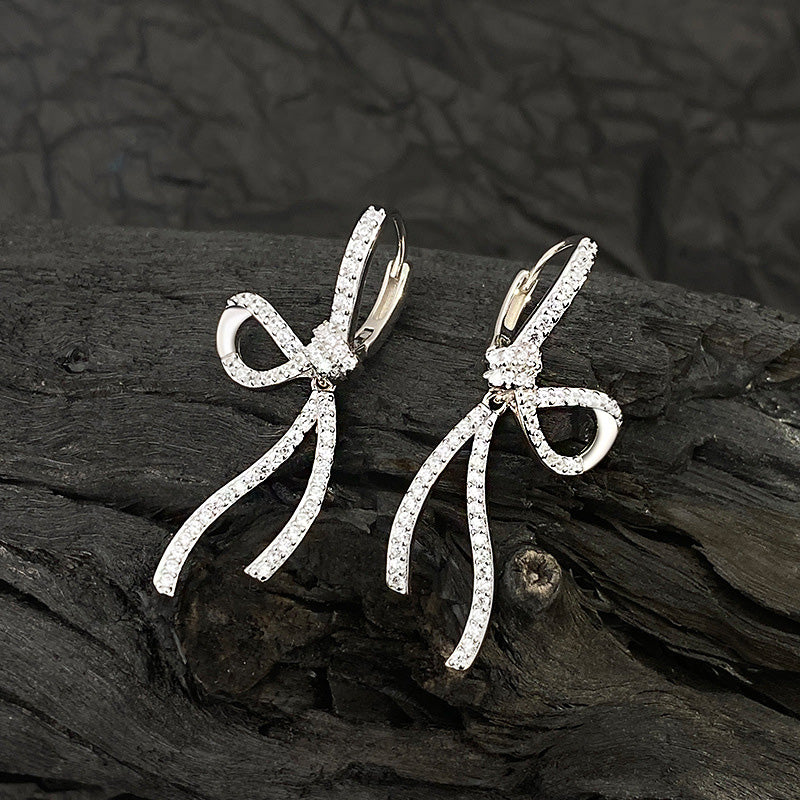 A pair of 925 sterling silver sweet CZ bow knot pierced earrings, showcasing the intricate design and sparkling white stones on a neutral background.