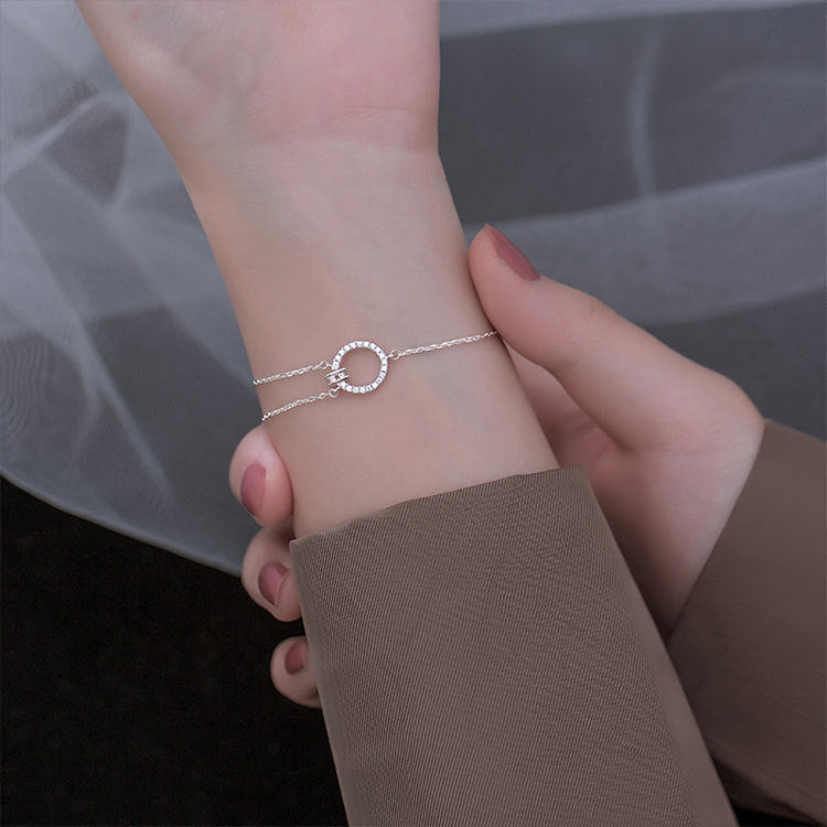 A close-up of a 925 sterling silver bracelet featuring an asymmetric chain and a geometric circular charm set with sparkling zircon stones.